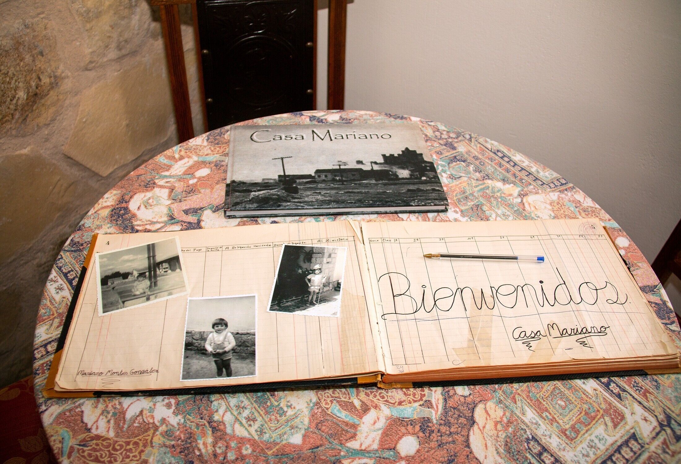 A notebook with 'Bienvenidos' and 'Casa Mariano' written on it, placed on a patterned tablecloth.
