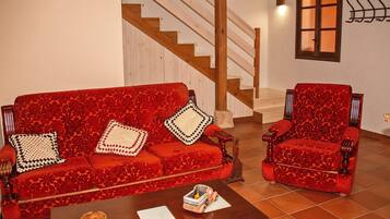 Un canapé et un fauteuil rouges à motifs dans une pièce dotée d’un escalier en bois et d’une fenêtre à vitre dépolie.