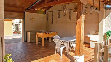 An outdoor patio with a wooden table and chairs, a foosball table, and a rustic wooden ceiling.