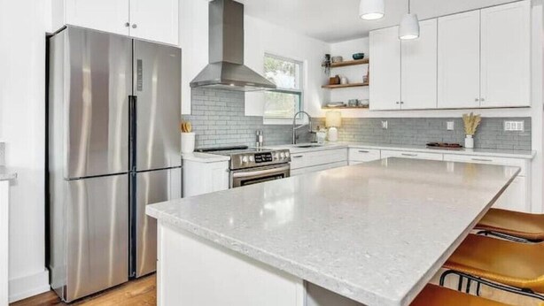 Una cocina moderna con armarios blancos, electrodomésticos de acero inoxidable y una isla central.