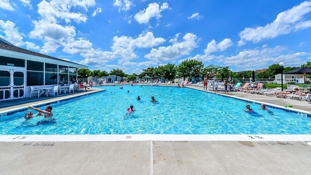 A swimming pool with people swimming and sunbathing, surrounded by lounge chairs and umbrellas. - Coastal Cottage - 2BR Home with 2 Pools, pond, & 1000ft pier in Assateague Point (Berlin)