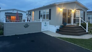 A single-story mobile home with a front porch, a small deck, and a fenced yard. - Coastal Cottage - 2BR Home with 2 Pools, pond, & 1000ft pier in Assateague Point (Berlin)