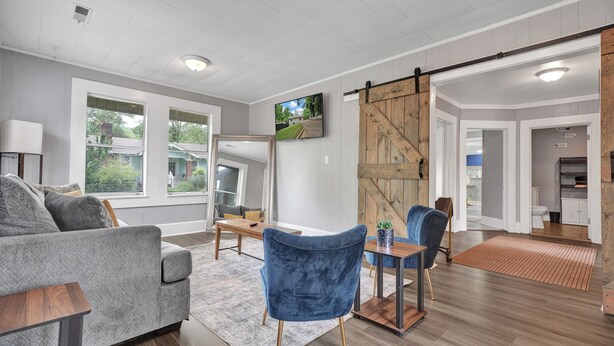A modern living room with a gray sofa, blue chairs, a wooden coffee table, and a sliding barn door. - 3-bedroom vacation home 12 mins from University of Alabama-Birmingham &Hospital (Birmingham)