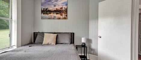 A bedroom with a bed, a nightstand, a lamp, a door, and a cityscape painting on the wall.