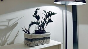 Una habitación con un escritorio blanco, una lámpara de pie, una planta en maceta y una rama en la pared.