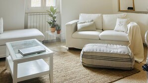 Un salón minimalista con un sofá blanco, una mesita de centro de cristal, un otoman con rayas y una lámpara colgante.