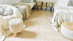Un dormitorio minimalista con dos camas, un taburete de madera y un otoman redondo.