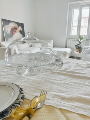 Une table à manger agrémentée d’un centre de table en forme de dôme transparent, d’une nappe blanche et d’un petit verre d’eau.