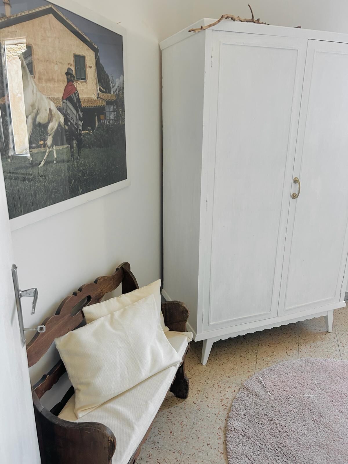 Habitació amb un armari blanc, una banca de fusta amb coixins i un quadre al mur.