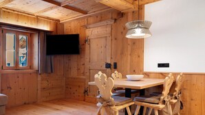 A wooden interior with a dining table, chairs, a television, and a whiteboard.