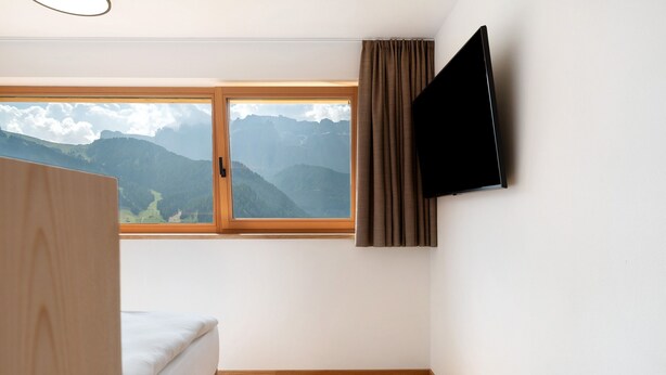 A room with a bed, a window with a mountain view, and a mounted television.