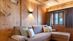 A wooden interior with a sofa, a wall-mounted light, and a window with curtains.