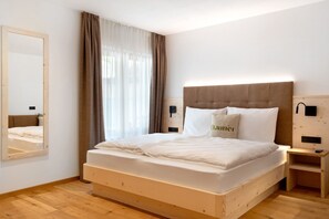 Un lit bien fait, avec une tête de lit, une table de chevet, une commode, un miroir et une fenêtre avec des rideaux.