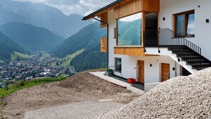 Une maison moderne dotée de grandes fenêtres, d’une façade en bois et offrant une vue sur une vallée et des montagnes.