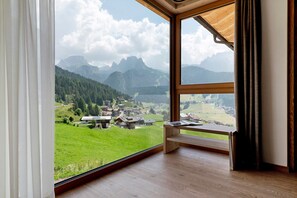 A room with a large window offering a view of a mountainous landscape and a village below.