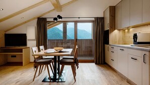 A modern kitchen with wooden cabinets, a dining table with chairs, and a large window with a mountain view. - Apartment 'Fën' with Mountain View, Shared Garden and Wi-Fi (Wolkenstein)