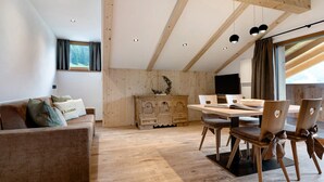 A modern interior with a wooden ceiling, a dining area with chairs and a table, a sofa with cushions, and a cabinet. - Apartment 'Fën' with Mountain View, Shared Garden and Wi-Fi (Wolkenstein)