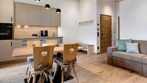 A modern kitchen with wooden cabinets, a dining table with chairs, a sofa, and a wooden floor. - Apartment 'Fën' with Mountain View, Shared Garden and Wi-Fi (Wolkenstein)
