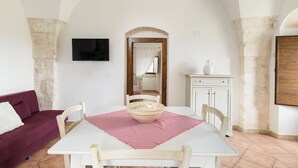 Uma sala de jantar com mesa, cadeiras, uma tigela, uma televisão e um sofá.