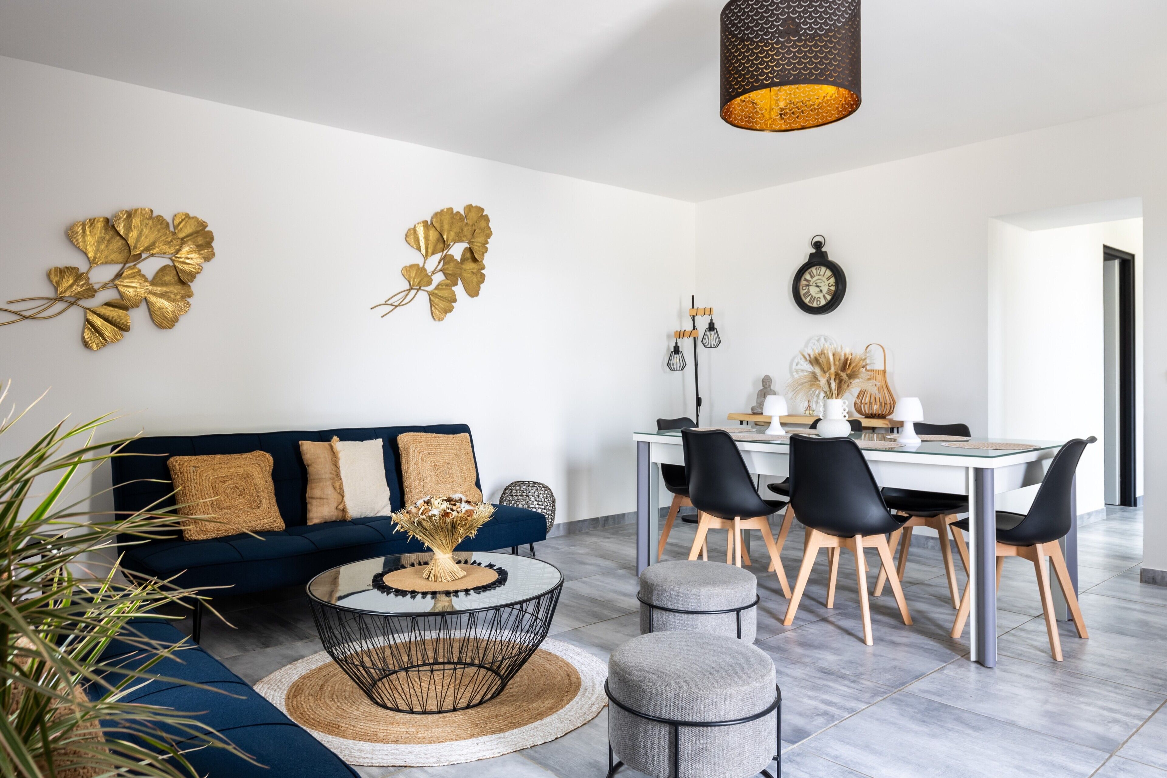 A modern living room with a dark blue sofa, a round coffee table, and a dining area with a white table and black chairs.