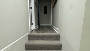 A narrow hallway with carpeted stairs leading to a door at the end. - Cozy 2-bedroom apartment in tranquil Nutter Fort with AC, WiFi. Close to I 79. (Clarksburg)