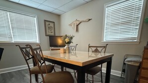 A dining area with a rectangular table, four chairs, a vase with flowers, a wall-mounted bird sculpture, and a television on a stand. - Cozy 2-bedroom apartment in tranquil Nutter Fort with AC, WiFi. Close to I 79. (Clarksburg)