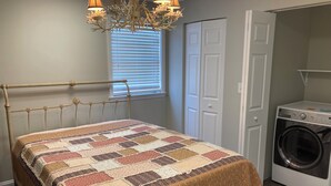 A bedroom with a bed, a chandelier, a window with blinds, a door, and a washing machine. - Cozy 2-bedroom apartment in tranquil Nutter Fort with AC, WiFi. Close to I 79. (Clarksburg)