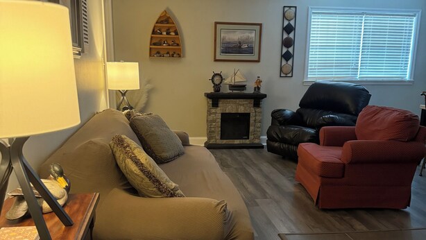 A living room with a sofa, a red armchair, a fireplace, and a window with blinds. - Cozy 2-bedroom apartment in tranquil Nutter Fort with AC, WiFi. Close to I 79. (Clarksburg)