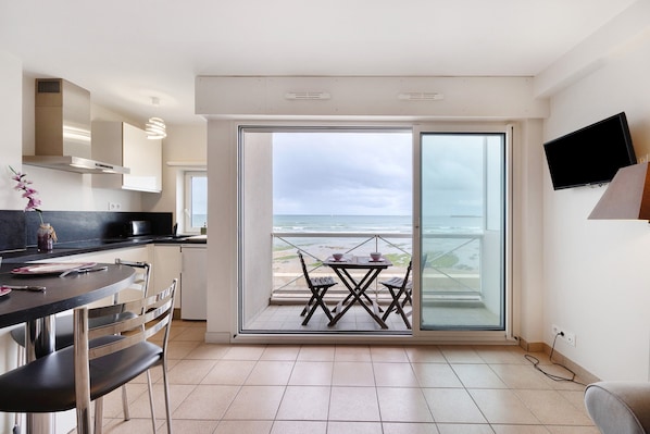 A modern kitchen with a dining area, a TV, and a balcony with a view of the sea.