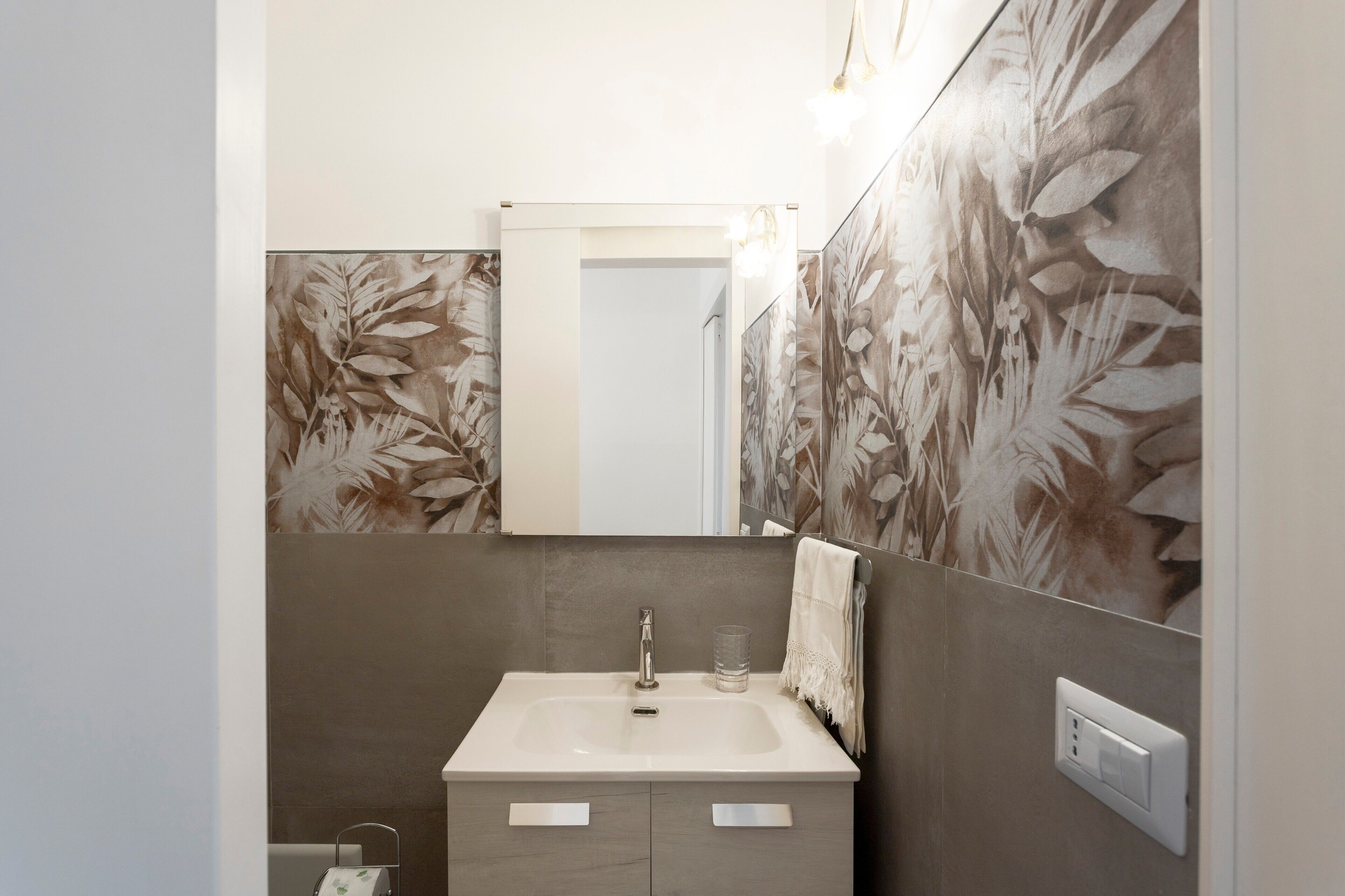 A bathroom with a sink, mirror, and floral wallpaper.