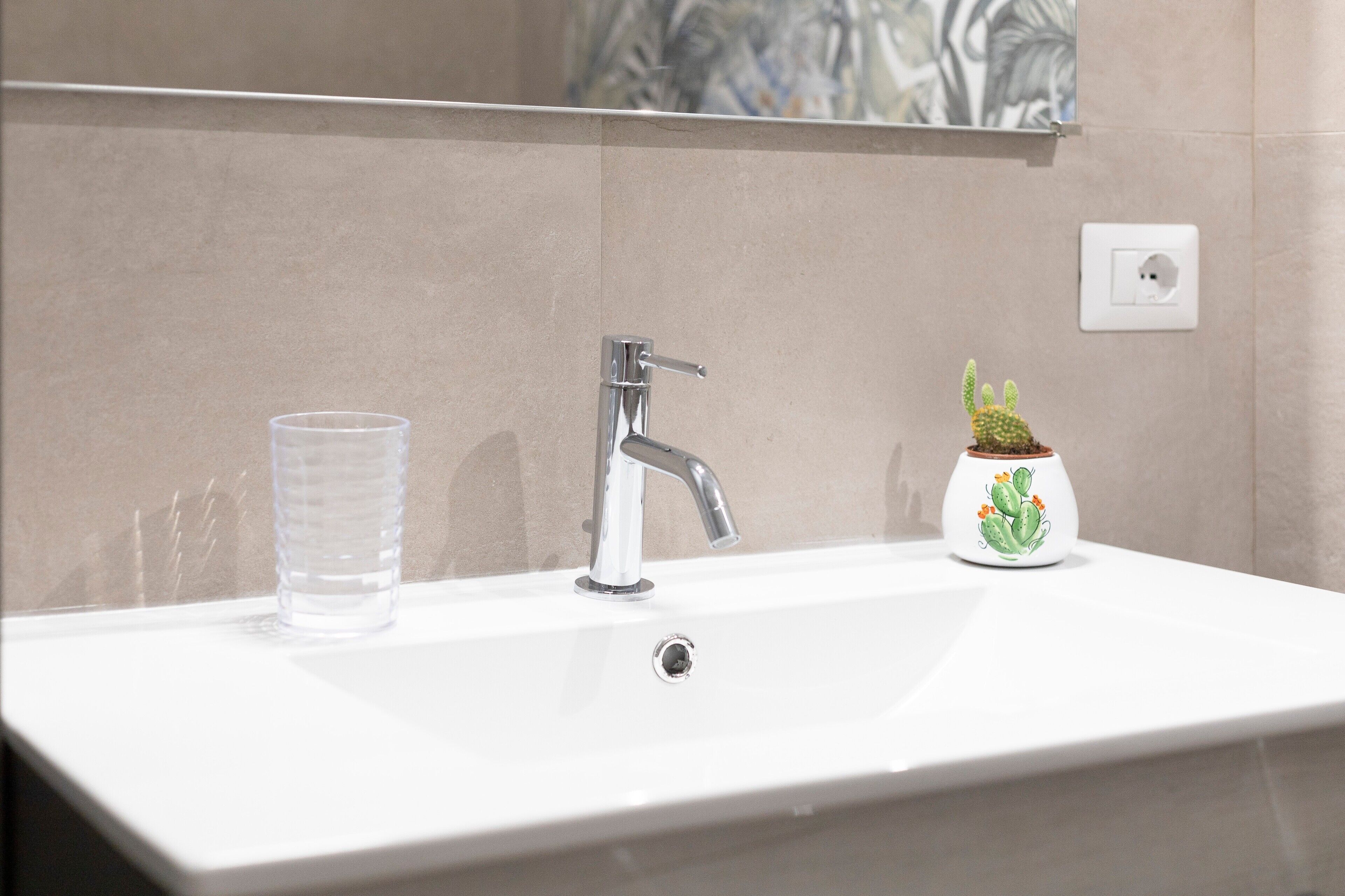 A bathroom sink with a faucet, a clear glass, and a cactus-shaped container.