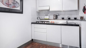 A modern kitchen with white cabinets, a gas stove, a sink, and a kettle.