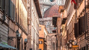 A narrow street with historic buildings, a prominent dome, and a clock tower.