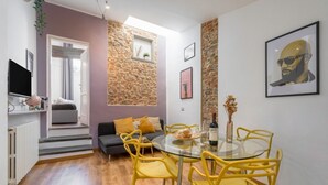 A modern living room with a stone accent wall, a round glass dining table with yellow chairs, a grey sofa with yellow cushions, and a television on a white cabinet. - Heart of Florence: Central, Cozy Apt with Elevator (Firenze)