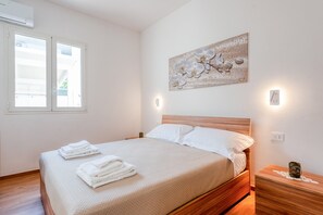 Une chambre à coucher comprenant un lit, une table de chevet, une lampe fixée au mur, une fenêtre et un tableau décoratif représentant une orchidée.