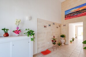 Un couloir orné de plantes en pot, avec un banc rouge, un tableau accroché au mur et un sol carrelé.
