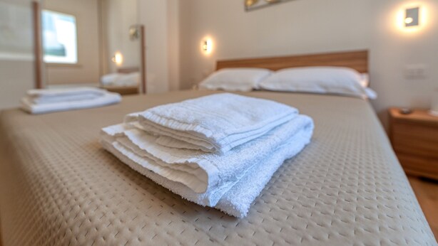 A neatly made bed with white towels, a wooden headboard, and a wall-mounted light fixture.
