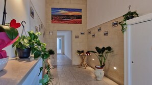 A hallway with potted plants, a painting on the wall, and a door at the end.