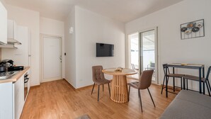 A modern kitchen with a built-in stove, a dining area with a round wooden table and two chairs, and a TV mounted on the wall.