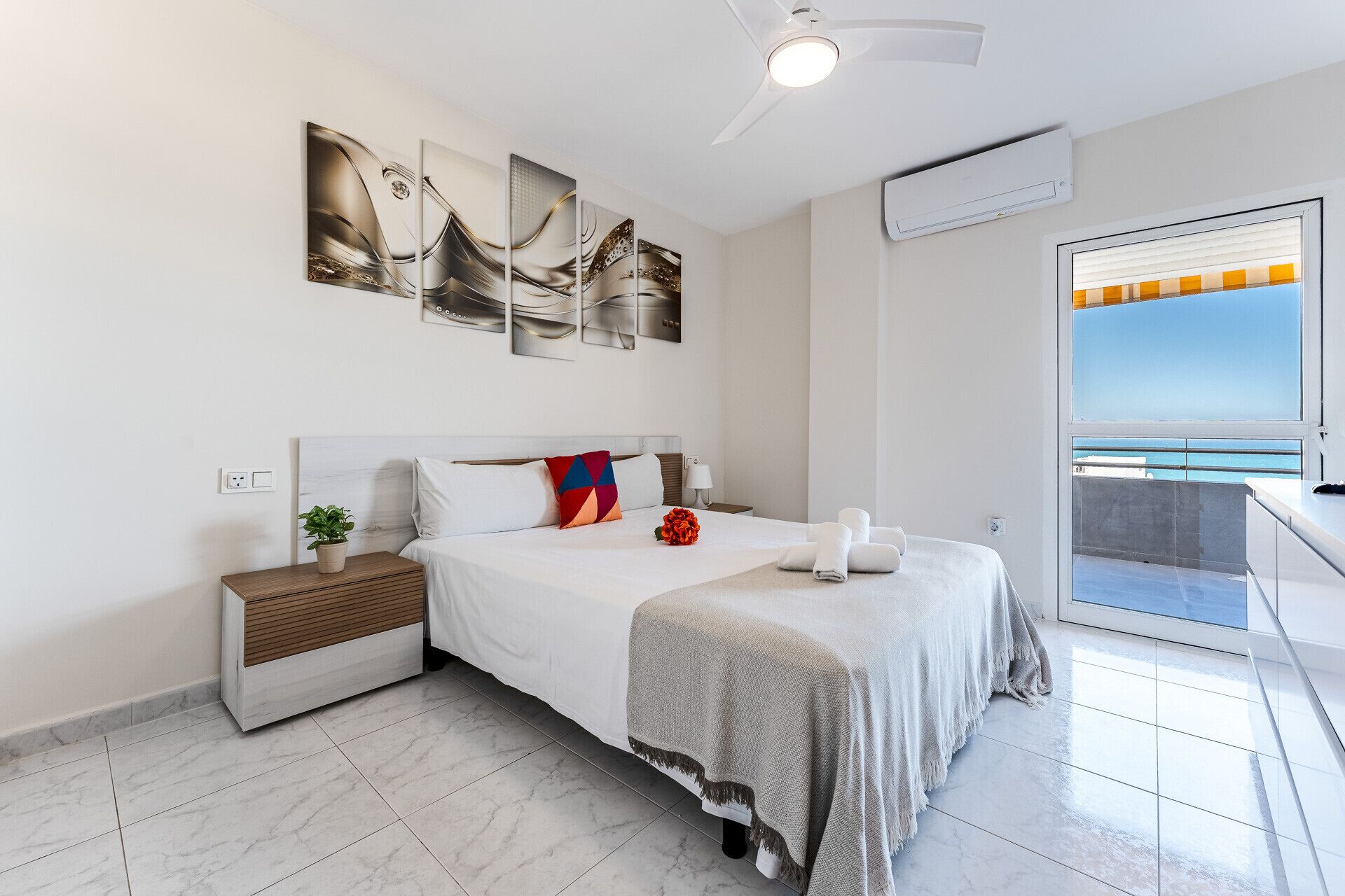 A modern hotel room with a bed, a nightstand, a potted plant, and a balcony with a view.