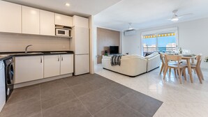 A modern kitchen with white cabinets, a microwave, and a built-in oven. There is a dining area with a white sofa and a table set for two. - MalagaSuite Seaview Babilonia (Torremolinos)