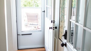 Un couloir doté d’un plancher en bois, d’une porte blanche avec des panneaux de verre et d’un luminaire fixé au mur.