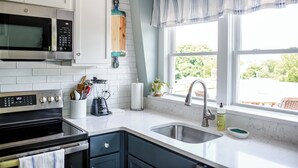 Une cuisine moderne avec des meubles blancs, un four à micro-ondes en acier inoxydable, un four encastré, un évier et une fenêtre donnant sur un espace verdoyant.