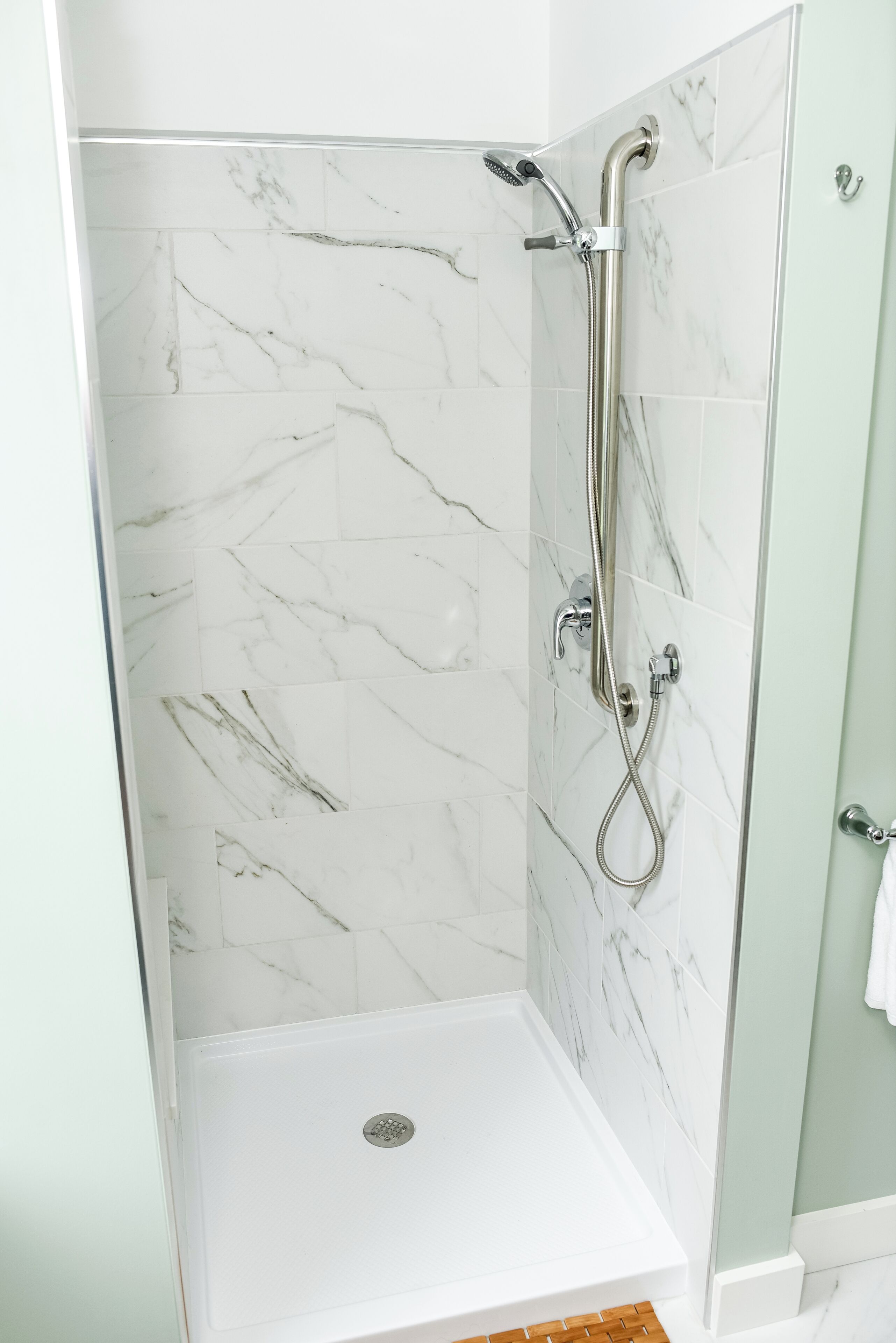 A walk-in shower with a glass door, white marble tiles, and a handheld showerhead.