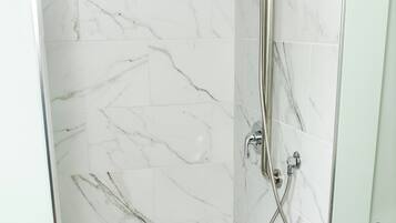 A walk-in shower with a glass door, white marble tiles, and a handheld showerhead.