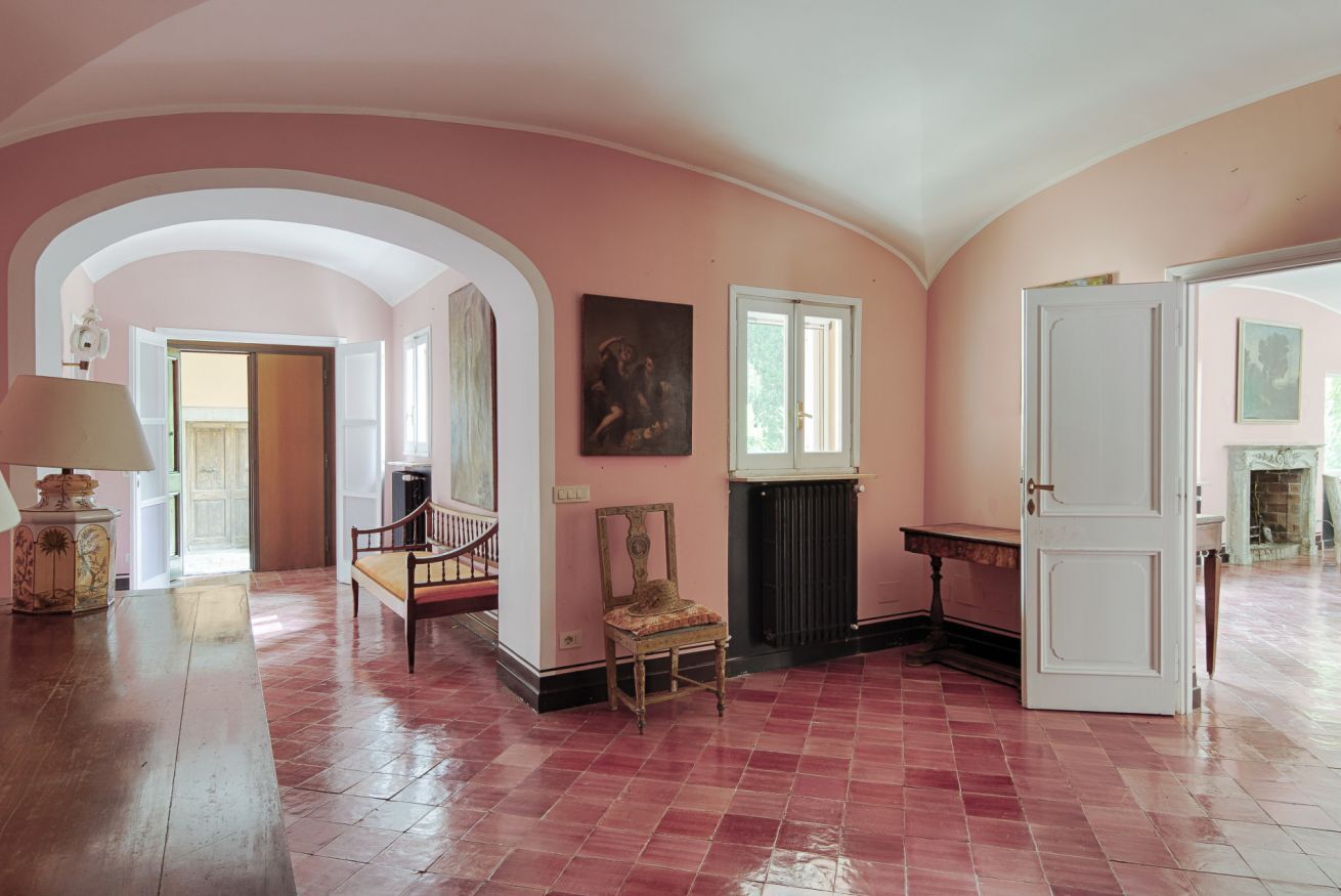 Ein geräumiger Raum mit hoher Decke, Kamin, großem Fenster und einer Tür zu einem anderen Raum.