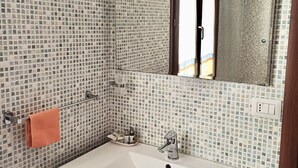 Un baño con paredes de mosaicos, un lavamanos, un espejo y un perchero para toallas.