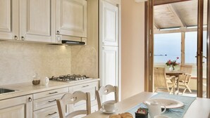 Una cocina con comedor, vista al mar y una mesa dispuesta con tetera, tazas y pasteles.