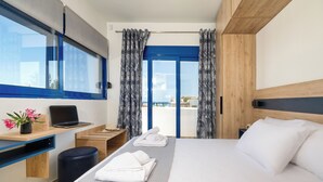 A modern hotel room with a bed, a desk with a laptop, a small stool, and a view of the sea through large windows. - Villa Mariani II (Rhodes)