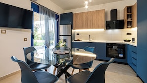 A modern kitchen with a dining area, featuring a glass table, blue chairs, and a built-in oven. - Villa Mariani II (Rhodes)